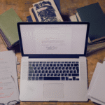 Computer and laptop with writing papers laying next to it